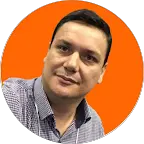 Retrato de homem sorridente usando camisa social, destacado contra fundo laranja vibrante em formato circular.